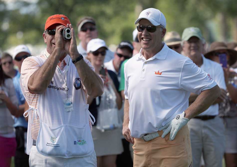 球童蹲在果岭边，手持测距设备，正全神贯注地为球员确认精准的击球距离。