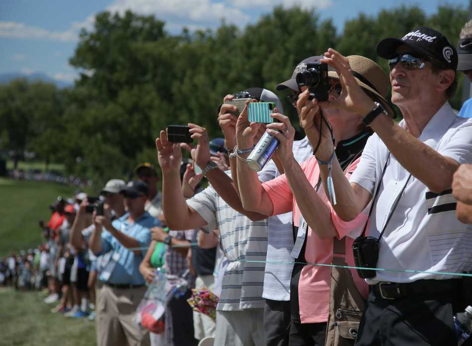 热情的球迷们聚集在围绳边，纷纷举起手机和相机，捕捉赛场明星的精彩瞬间。