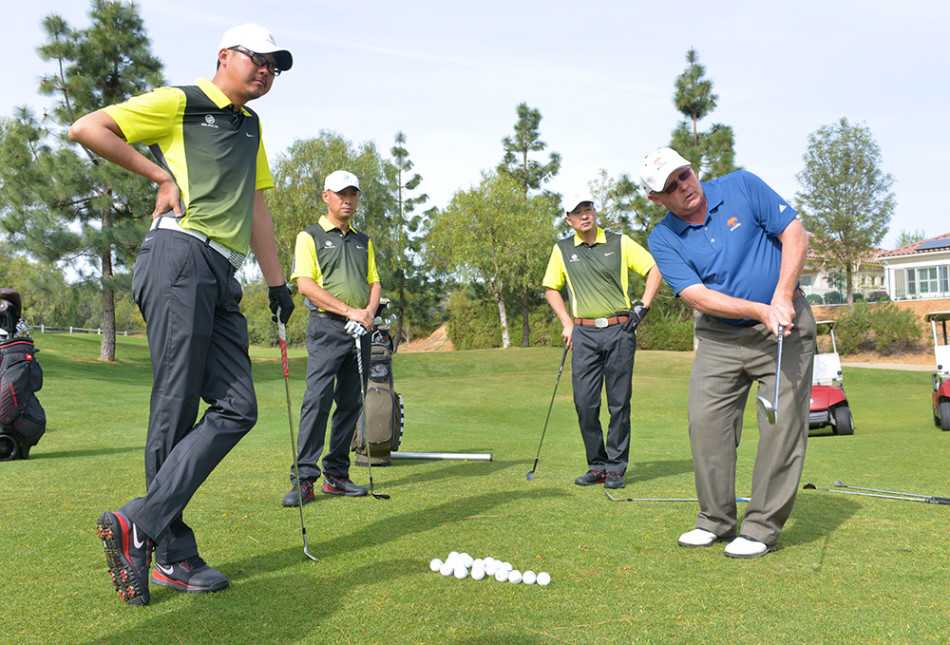 教练保罗在果岭旁侧身演示短杆挥杆，阳光将他的专注身影拉长，手中的挖起杆定格在完美的上杆顶点