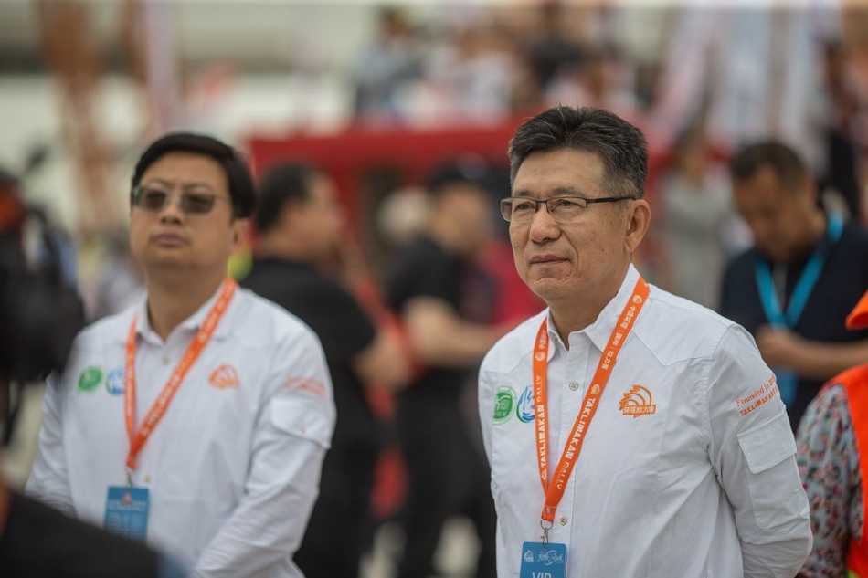 瀚海逐梦·引擎轰鸣——二〇二三年环塔拉力赛开幕盛典纪实 发车台上,车手与领航员紧握拳头高举双臂,身后是色彩斑斓的参赛车辆,激情与信心在蓝天黄沙间澎湃激荡。