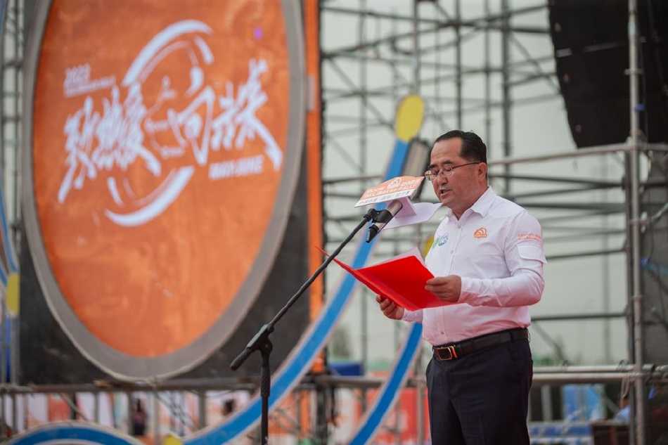 瀚海逐梦·引擎轰鸣——二〇二三年环塔拉力赛开幕盛典纪实 一辆喷涂着火焰图案的红色赛车飞跃而起,车身在空中划出凌厉的弧线,四溅的沙粒在逆光中宛如金色的星尘。