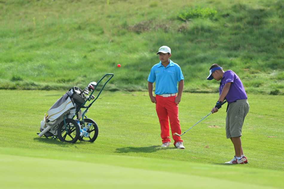 果岭边的博弈与情谊青少年高尔夫赛事中的专注时刻与团队精神 年轻高尔夫球手在果岭边缘全神贯注地准备切杆,试图将球精准地送到洞口附近。