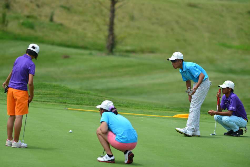 果岭边的博弈与情谊青少年高尔夫赛事中的专注时刻与团队精神 高尔夫球员正俯身仔细观察果岭上的推杆线路,神情专注,不放过任何可能影响球路的细节。