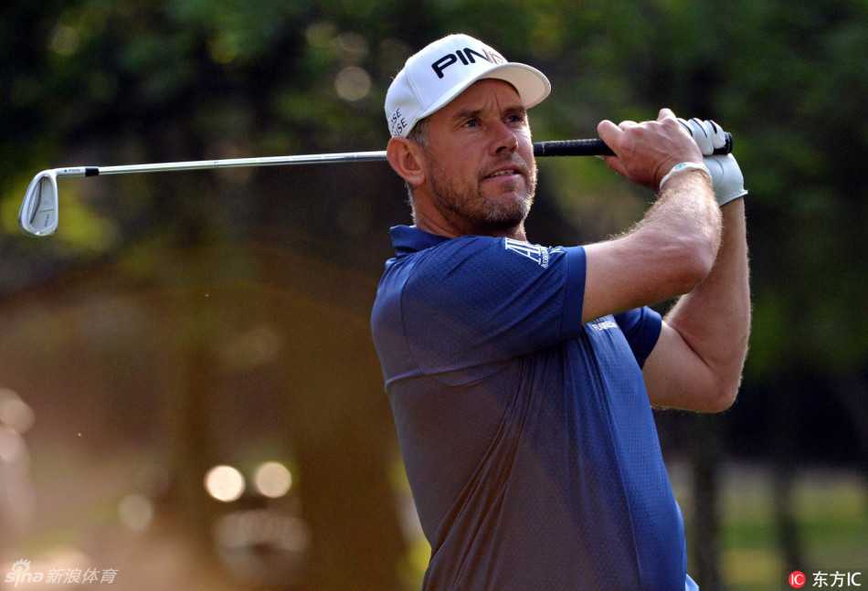 镜头追随高尔夫球在空中飞向远方的轨迹，背景是火石球场经典的树林球道，画面充满动感与期待。