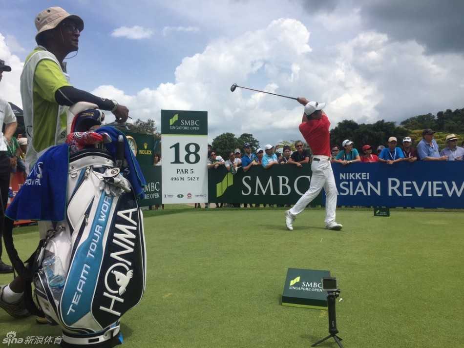 梁文冲在练习场调整挥杆动作，背景中可见其他选手正在备战