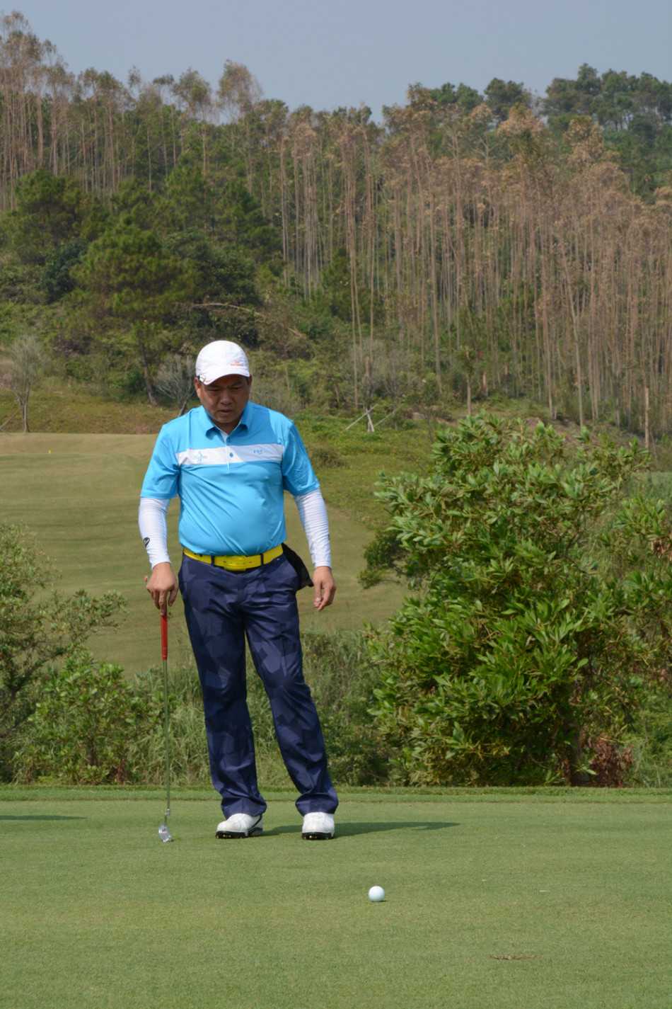 球员在果岭边屈膝半蹲，聚精会神地观察草纹走向与坡度，为关键一推做最后的计算与思考