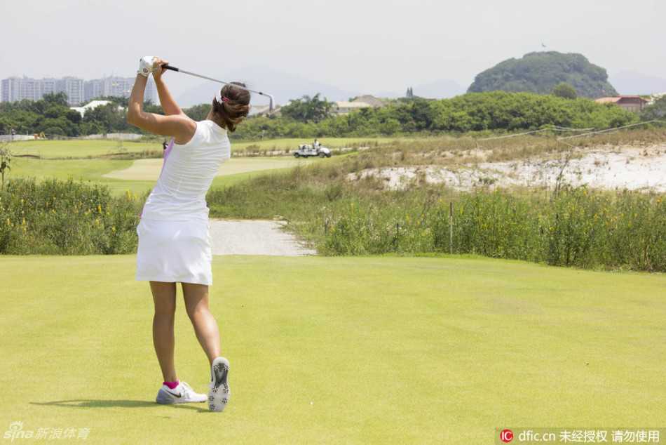 比赛进行中，球员与球童走在开阔的球道上，背景可见独具特色的沙坑与远山，展现奥运球场的壮丽景观。