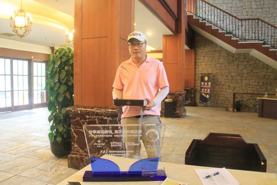 一位笑容满面的球手正从工作人员手中郑重接过精美的‘百鸟争鸣’礼盒，完成胜利时刻的荣耀授予。