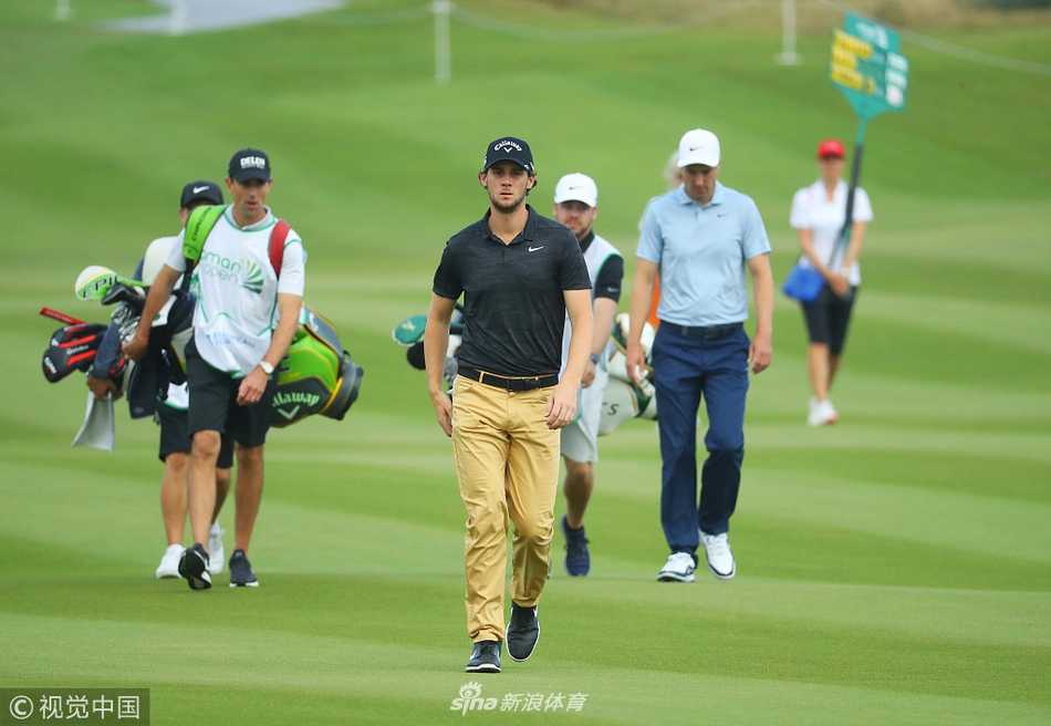 罗斯-费舍尔在巨大沙坑中挥杆，沙粒如瀑布般溅起，背景是湛蓝的阿曼海湾。