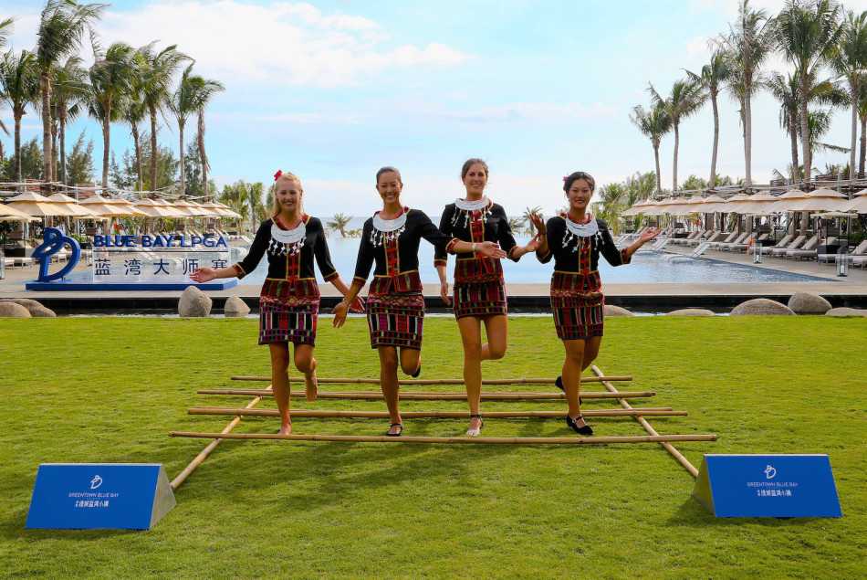 四位高尔夫女将完成竹竿舞体验后开心合影，背景是海南标志性的椰林与蓝天