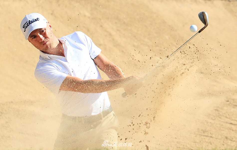 贾斯汀·托马斯在果岭边审慎观察推杆线路，阳光将他的身影拉长，突显出比赛的关键时刻。