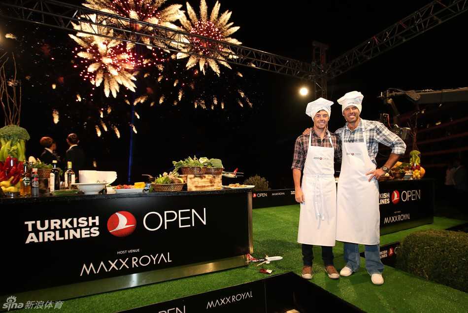 麦克罗伊与舒瓦泽尔身着围裙，在现代化的厨房中相对而立，准备展开一场友谊厨艺对决，两人脸上都带着轻松的笑容。