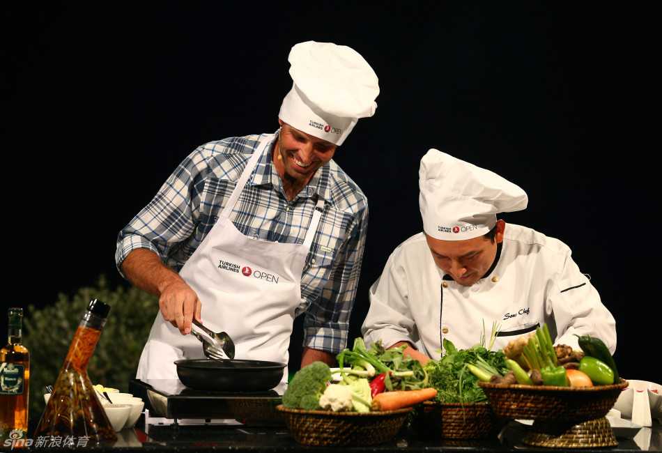 专业厨师正在耐心指导麦克罗伊，手指向食材进行讲解，麦克罗伊身体微微前倾，听得十分认真。