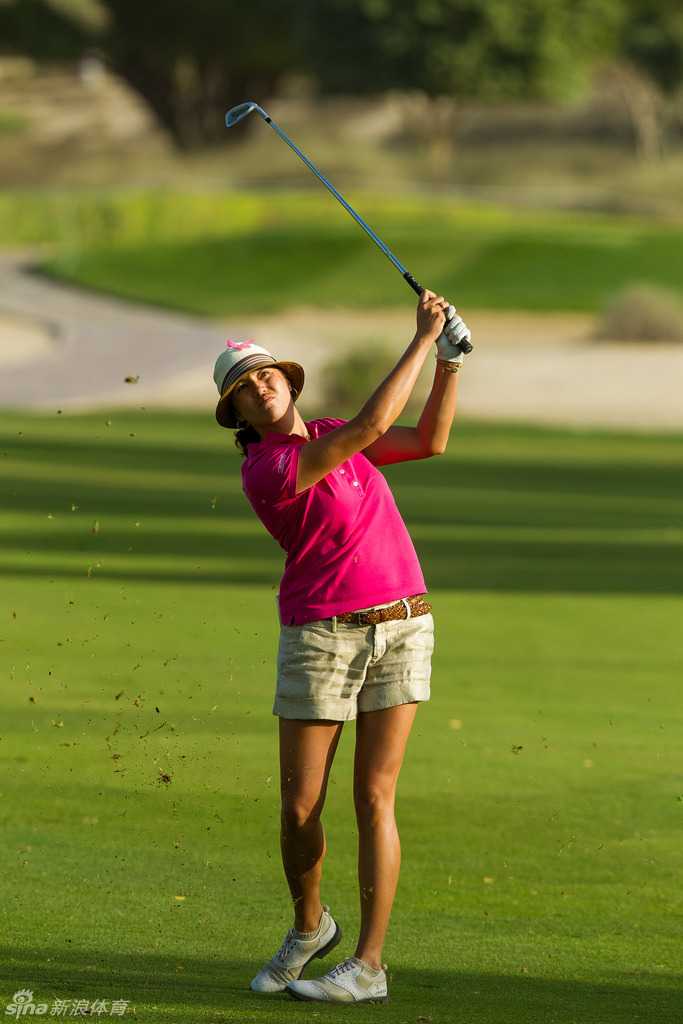 球员与工作人员在练习果岭上交流，众人衣着中的红色与粉色元素相互映衬，气氛轻松而融洽。