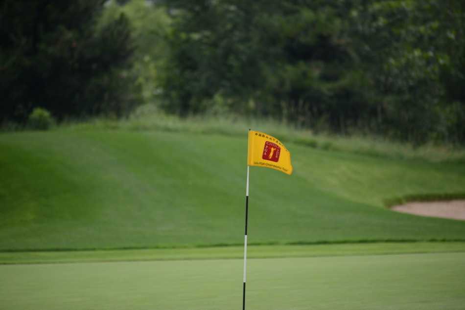 绿茵挥杆风尚尽显 天然苏打水润泽高球雅集 一面鲜艳的果岭旗在湛蓝天空下迎风招展,旗杆笔直插在修剪整齐的果岭上,周围是起伏的地形,意境悠远。