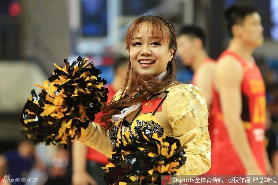 镜头拉近，两位篮球宝贝面对面站定，她们上身穿着白色紧身露脐背心，下身搭配蓝色热裤，展现出健康的小麦色肌肤和马甲线。她们正摆出一个充满力量感的定格姿势，眼神自信地望向远方的看台。