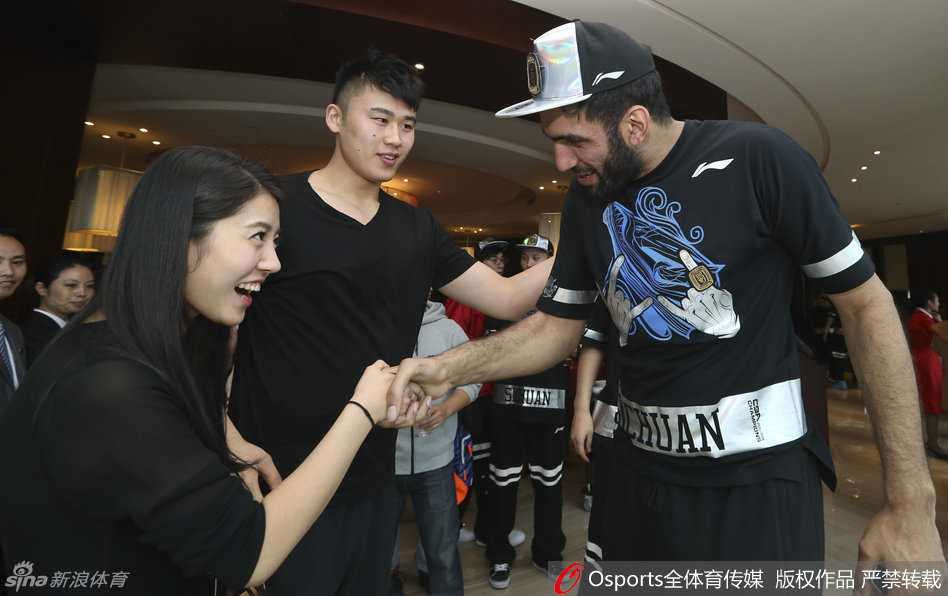 身穿制服的气质空姐化身小粉丝，在哈达迪身边仰头微笑，哈达迪则绅士地弯下腰，轻轻握住女球迷的手，画面温馨而有趣。