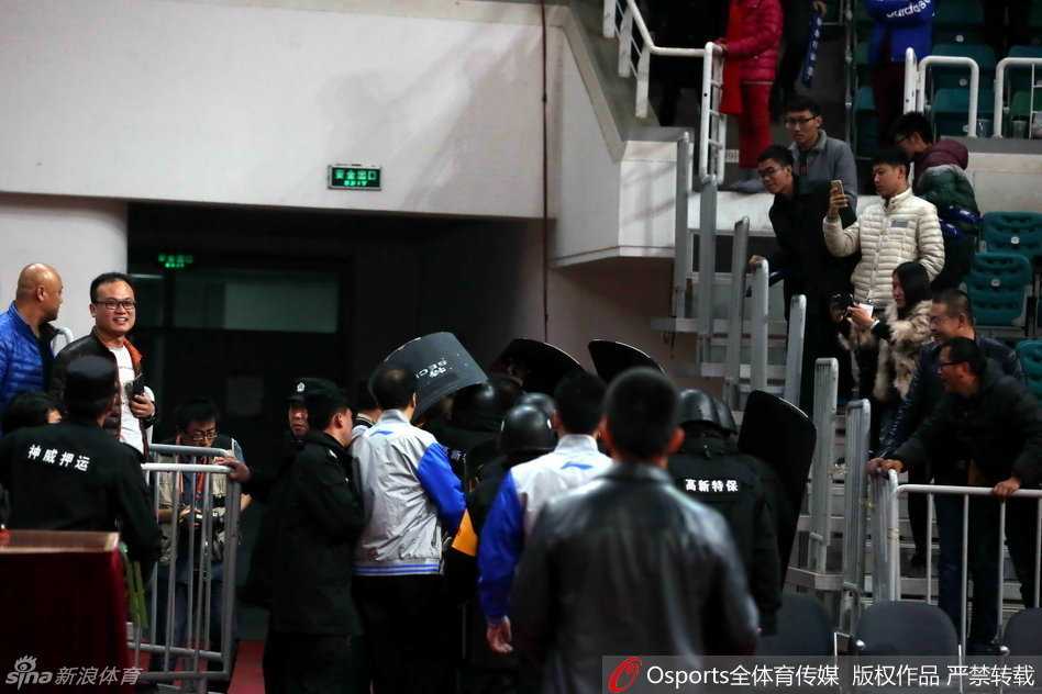 京晋大战硝烟散尽 安保筑起最后防线 在安保人员的层层护卫下,裁判员低着头快步疾走,试图快速穿过球员通道入口,身后的背景是模糊不清但又充满压迫感的看台人群。