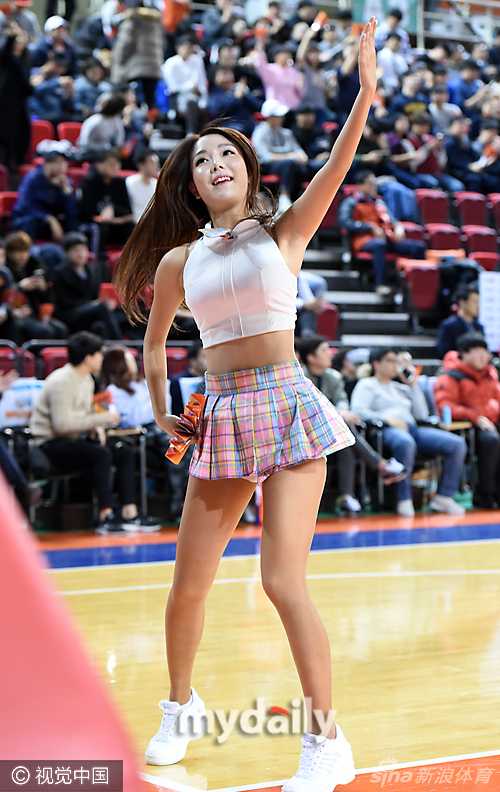 镜头拉近，这位啦啦队员在舞动的间隙轻轻撩起秀发，眼神中透露出一种专业的从容与自信。身后的队友虽然虚化，但依然能看出她们保持着整齐划一的队形，共同构成一幅动感十足的画面。