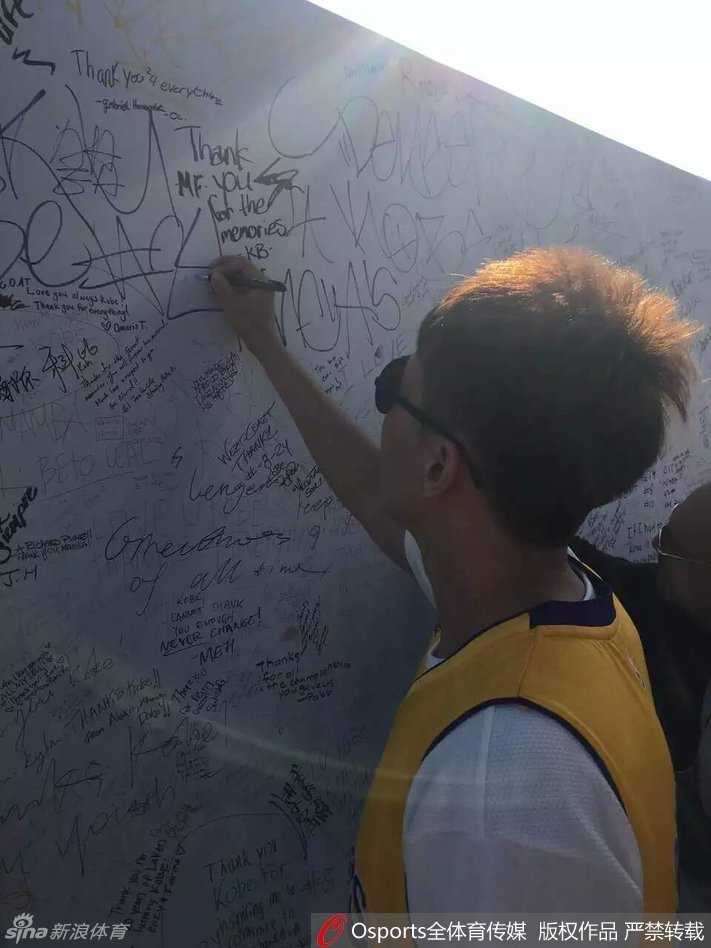 斯台普斯中心外，人潮涌动，曾令旭身穿醒目的紫金24号球衣，在科比的巨幅海报前停下脚步，眼神中满是期待与崇敬，用手机记录下这即将圆梦的一刻。