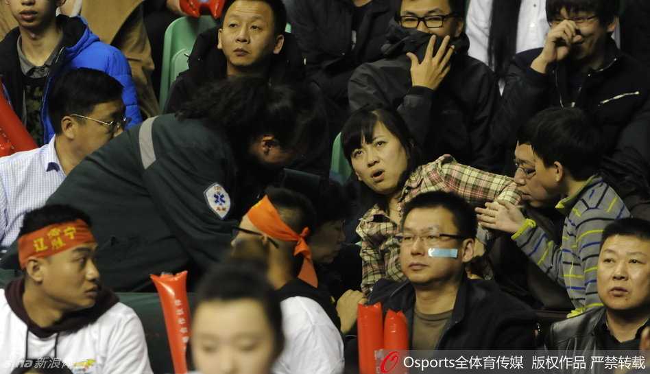 赛场紧张气氛令人窒息，一位女球迷在看台上突然失去意识晕倒，周围观众纷纷投来关切与焦急的目光。