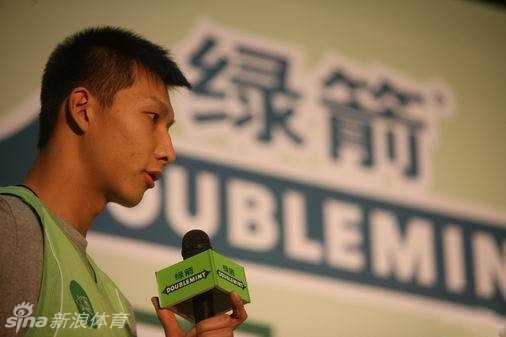 一只手从时尚的粉色烟盒状包装中抽出一片绿箭口香糖，背景是朋友聚会的模糊场景，突出了分享与亲近的社交瞬间。