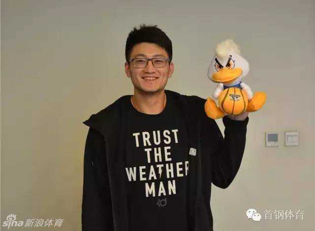 段江鹏加盟北京首钢后，面露羞涩而坚定的微笑，双手紧握象征京城荣耀的霹雳鸭吉祥物，仿佛握住了崭新的未来。