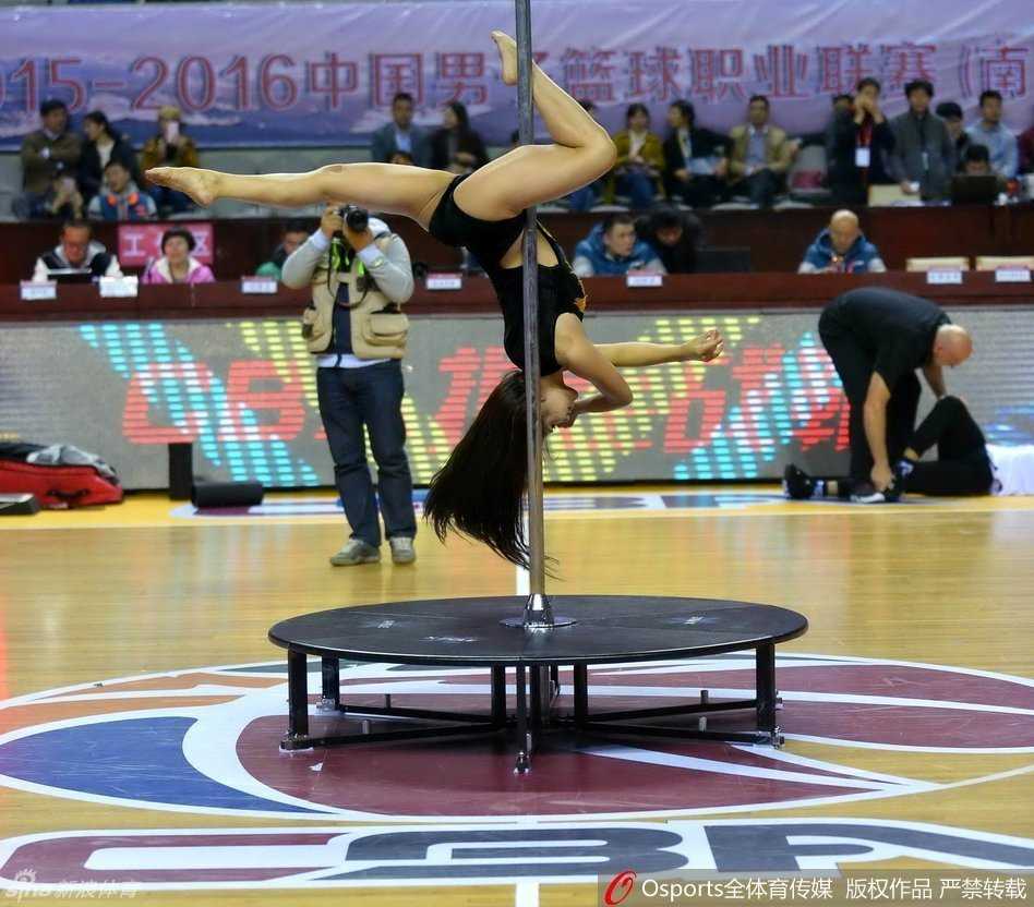 光影定格的瞬间，钢管舞女郎与远处的篮球架构成一幅奇妙的画面，竞技体育的刚硬与艺术表演的柔美在此刻交汇，成为CBA赛场娱乐化改革的一个注脚。