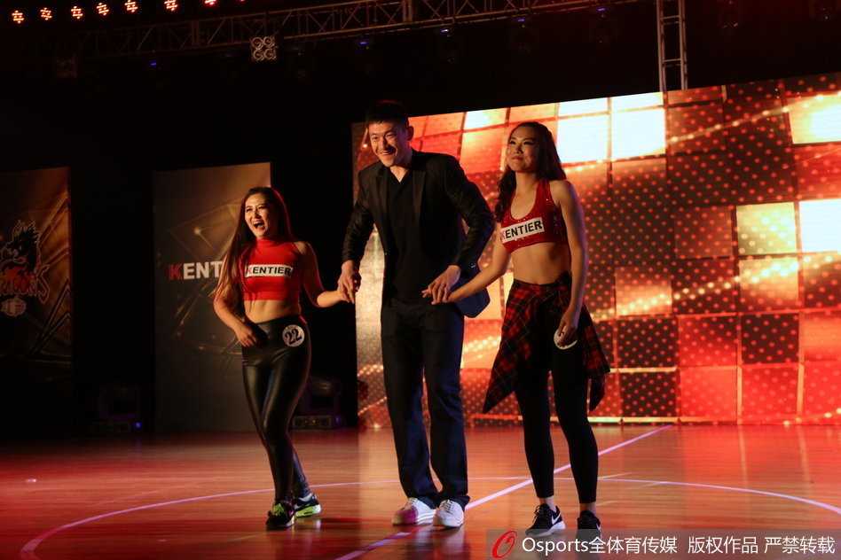 全体篮球宝贝与球队吉祥物在舞台上合影留念，她们摆出自信的pose，背后是巨大的江苏肯帝亚队徽。这一刻，美丽与力量完美融合，共同守护着江苏篮球的荣誉。