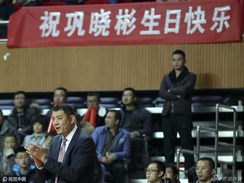 生日夜的遗憾与温情:巩晓彬在青岛球迷祝福中品味篮球人生 巩晓彬在赛后面带微笑地向球迷致意,他身边围绕着多名青岛队的球员,大家虽然没有赢球,但依然手拿球迷赠送的礼物,共同感受着来自支持者的温暖,背景是潍坊学院体育馆的通道。