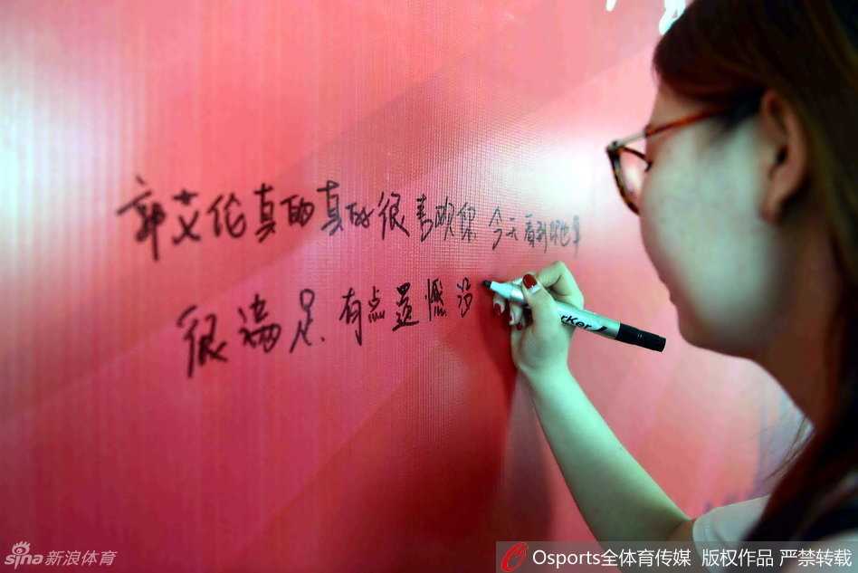 一位长发披肩的女球迷微微低头，手中紧握着一张写满真挚话语的纸条，眼神中流露出掩饰不住的失落与不舍，仿佛在默默祈祷偶像能看见这份心意。