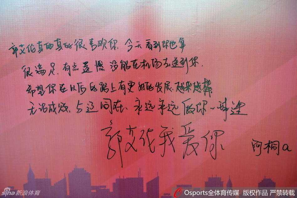 另一位戴着眼镜的女球迷，双手展开一张精心装饰的硬纸板，上面用荧光笔写着
