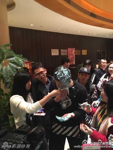 球迷们围在酒店大堂，手中捧着精致的蓝色生日蛋糕，烛光映照着一张张期待而温暖的笑脸