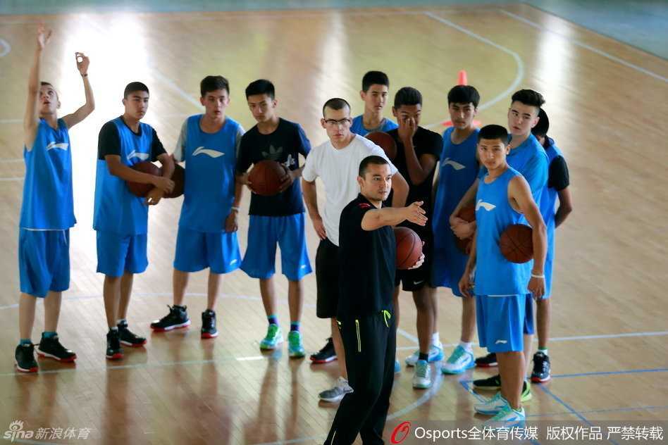 西热力江来到篮下做示范，他微微屈膝，双手抱球，正准备向小学员展示标准的投篮动作