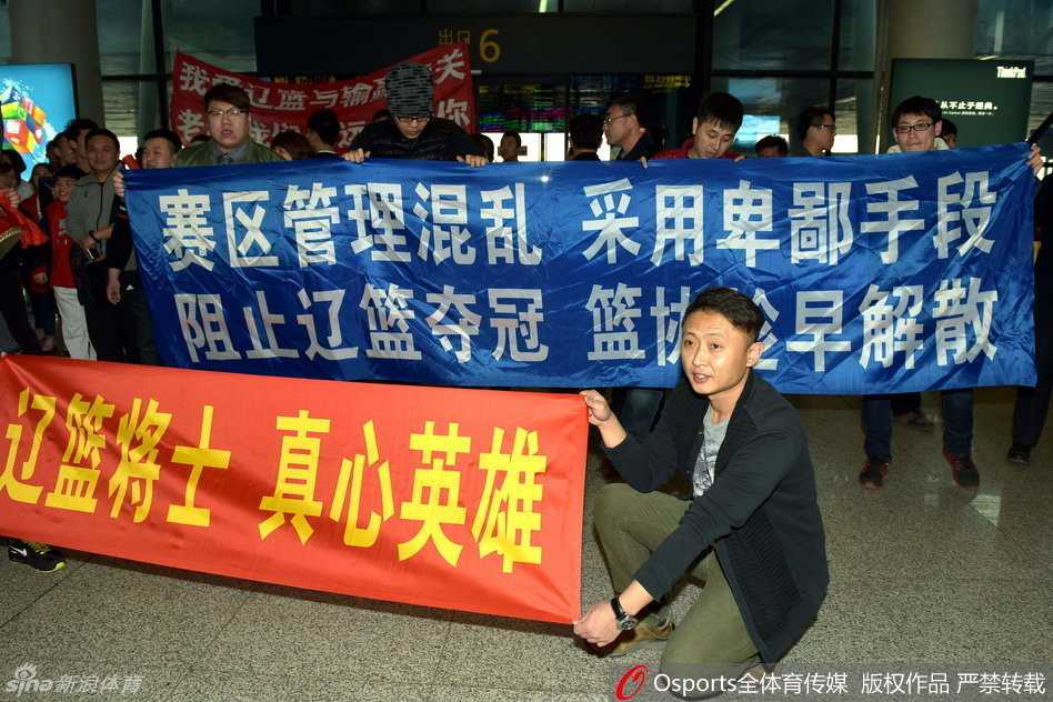 在拥挤的人群中，辽宁男篮主教练郭士强被特警和安保人员紧紧护在中间，他面色凝重，望着不远处那些举着支持标语却无法靠近的球迷们。