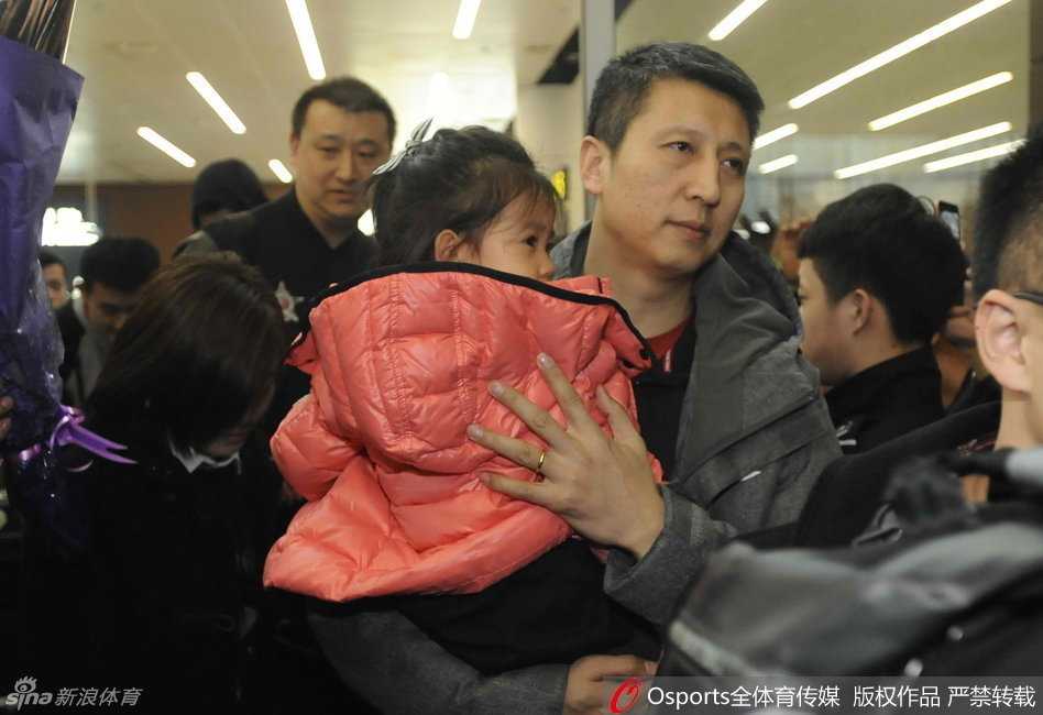 凯旋而归的辽篮主帅郭士强，怀抱自己可爱的女儿，脸上洋溢着铁汉柔情的幸福笑容。一旁的弟子们也被这温馨的一幕感染，眼神中充满了喜悦与放松。