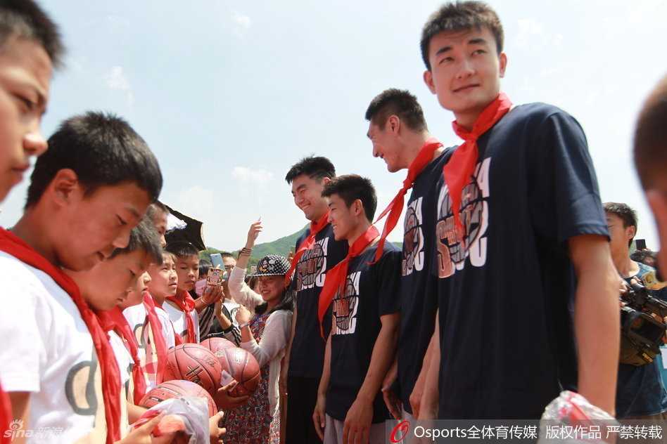 辽宁飞豹男篮全体将士与李大堡小学的师生们站在一起，在校园教学楼前拍摄大合影，所有人都面带笑容，气氛融洽。