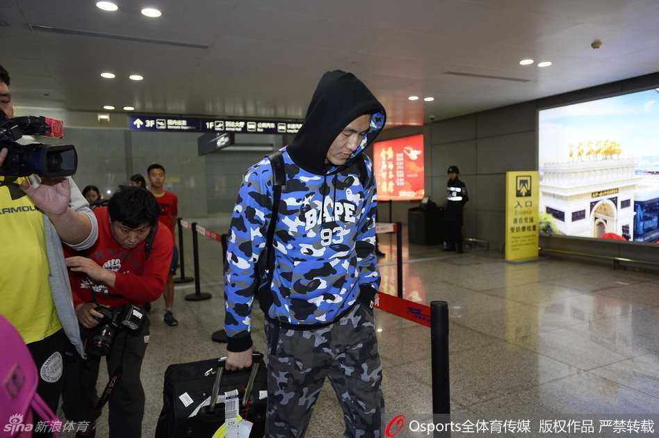 铁血柔情与创可贴的印记:辽篮三将成都归队记 一名戴着眼镜的辽宁女球迷,脸颊上同样贴着一块蓝色创可贴,她双手举着手机,眼神热切地望向正在走来的球员,脸上满是兴奋与期待。