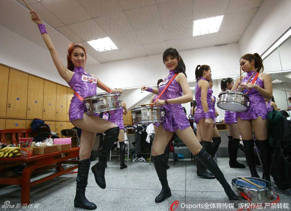 一位篮球宝贝正对着更衣室的镜子仔细补妆，手中的粉扑轻轻按压脸颊，身旁的队友则全神贯注地凝视着镜头，仿佛在等待上场音乐响起的那一刻。