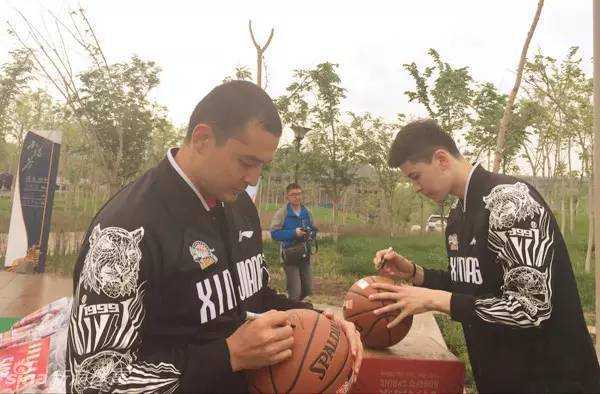 西热力江俯身给手中的篮球签名，他签得非常投入和细致，希望通过这颗篮球传递更多的爱心与正能量。