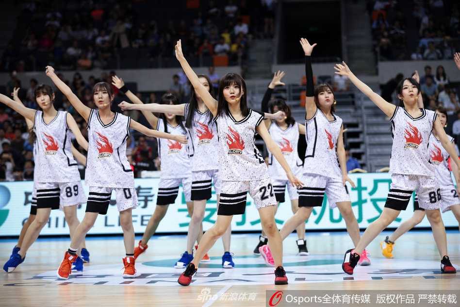 GNZ48助阵广东宏远豪取六连胜,青春风暴燃爆东莞篮球中心 镜头特写一位GNZ48成员,她手持啦啦队花球,专注的眼神中透露出对舞台的热爱,背后是宏远主场巨大的LED屏和热情的观众席。