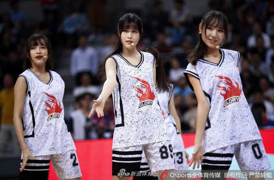 GNZ48助阵广东宏远豪取六连胜,青春风暴燃爆东莞篮球中心 一名GNZ48成员在赛场边回眸一笑,长发飘飘,身着紧身球衣勾勒出青春的身形,与身后专注观赛的球迷形成有趣的互动画面。