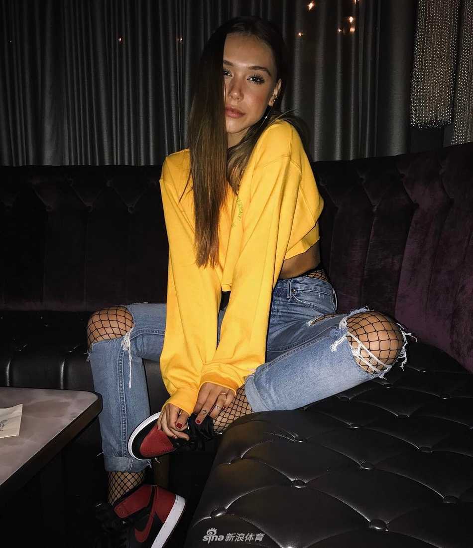 Alexis Ren身处洛杉矶的街头涂鸦墙前，她穿着高腰牛仔裤，上身是一件简约的白色Crop Top，露出紧实的马甲线，脚上的亮色AJ成为全身穿搭的焦点，尽显美式街头的随性与自信。