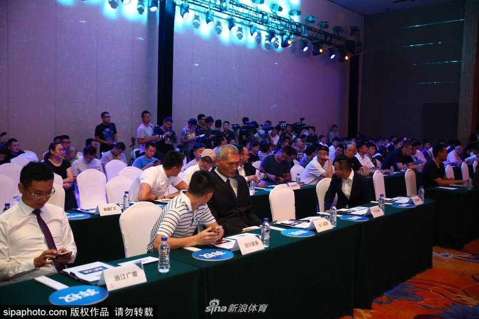 台上主持人正在宣读选秀结果，背后的大屏幕闪烁着各队LOGO，姚明在台下双手交叉于身前，神情严肃地注视着这一切，仿佛在守护着选秀大会的神圣。