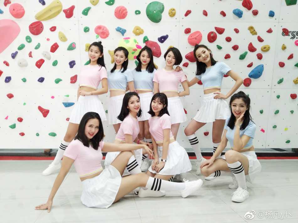 一位青春洋溢的空姐啦啦队员在球场边回眸一笑，马尾辫随着动作轻盈摆动，身后是正在热身的企业篮球队员