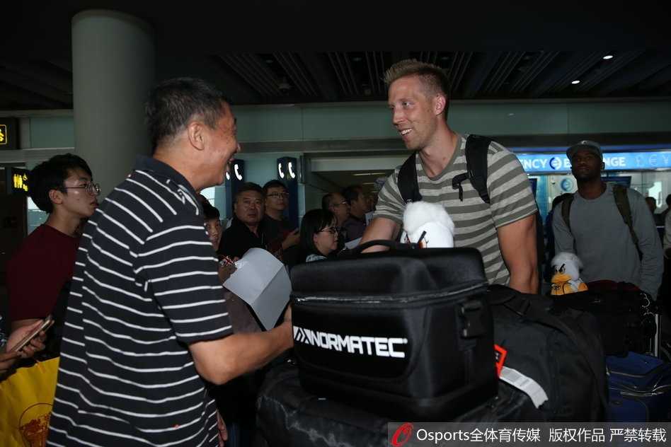 汉密尔顿在机场耐心地给一位小球迷签名，他微微弯腰，神情专注，阳光透过落地窗洒在他身上，勾勒出一幅温馨的画面。