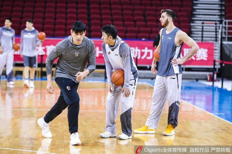 马布里身穿灰色训练服在场边进行拉伸，背景中可见北控队友们正在进行折返跑，大战前的宁静与紧绷感在空气中弥漫。