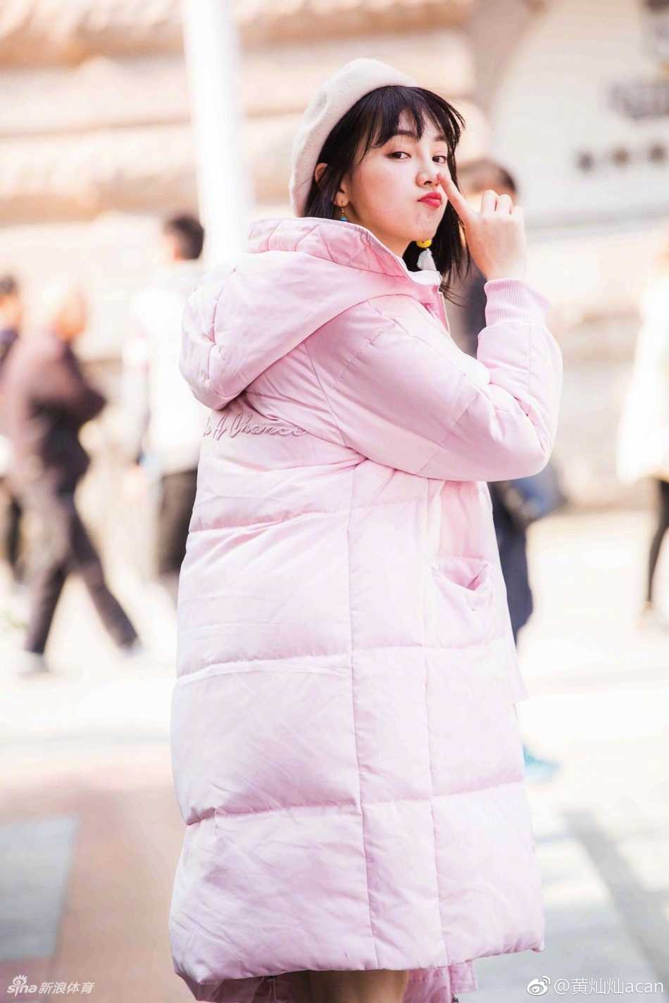 黄灿灿身着简约白色T恤，单手托腮凝视远方，身后是模糊的球场背景，神情专注而若有所思。