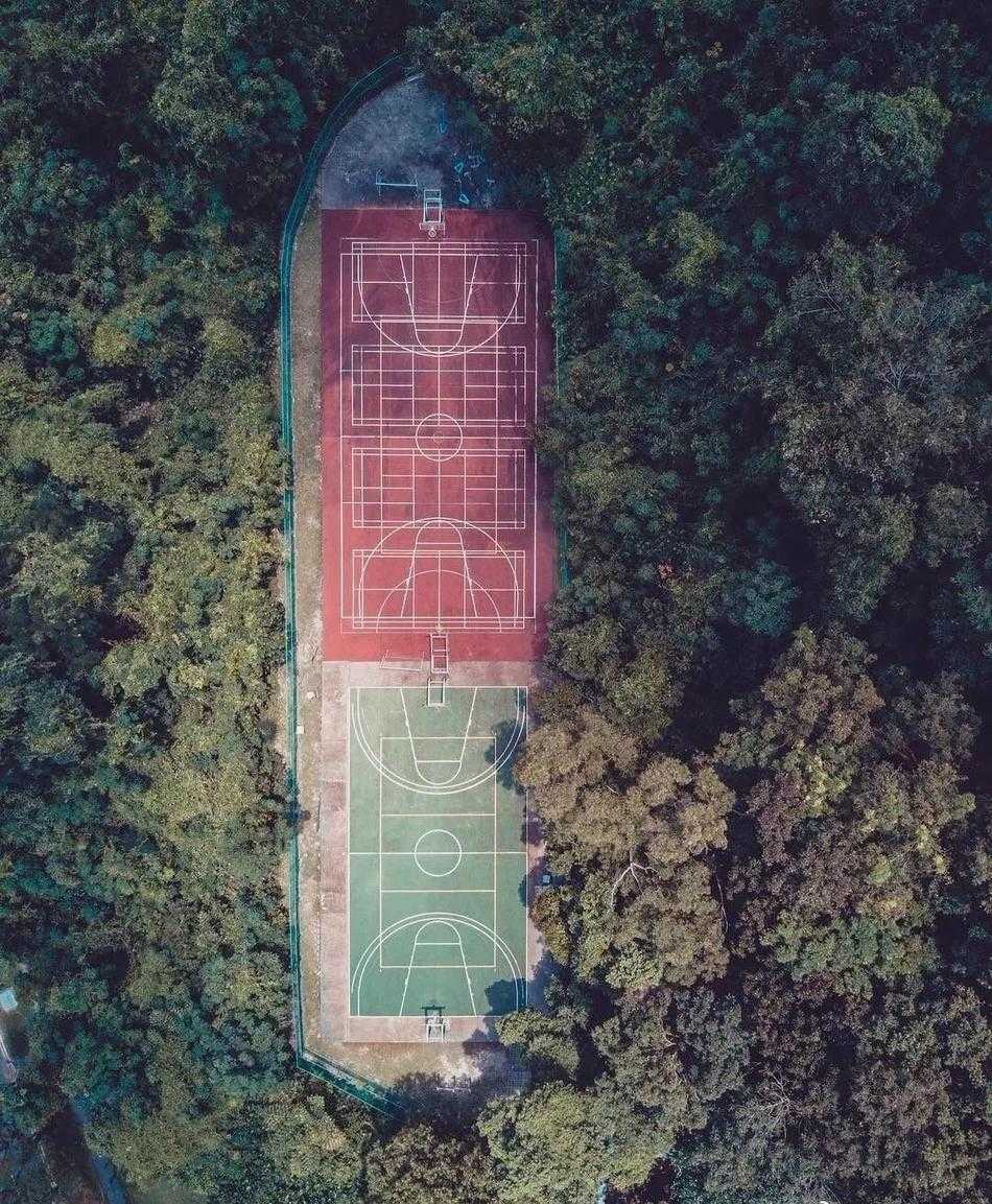 俯瞰光影交错,探寻篮球场的几何诗意 雨后,篮球场低洼处积水如镜,倒映出天空的晚霞和静止的篮架,现实与倒影虚实莫辨,营造出超现实的静谧美感。