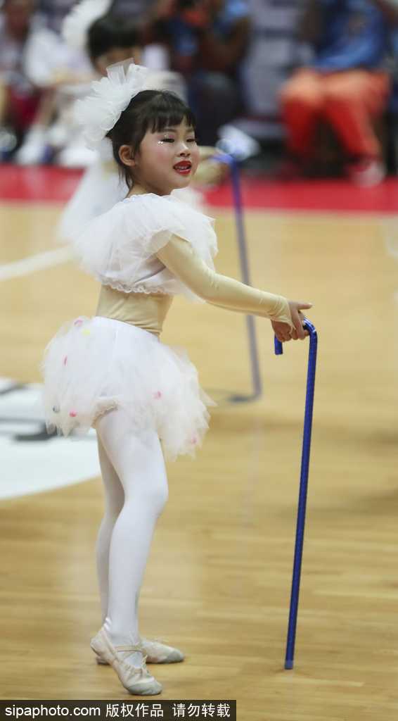 一位篮球宝贝蹲在地上，双手托腮，身旁放着彩色的小拐棍，一双会说话的大眼睛望向镜头，俏皮又无辜的表情简直萌翻了。